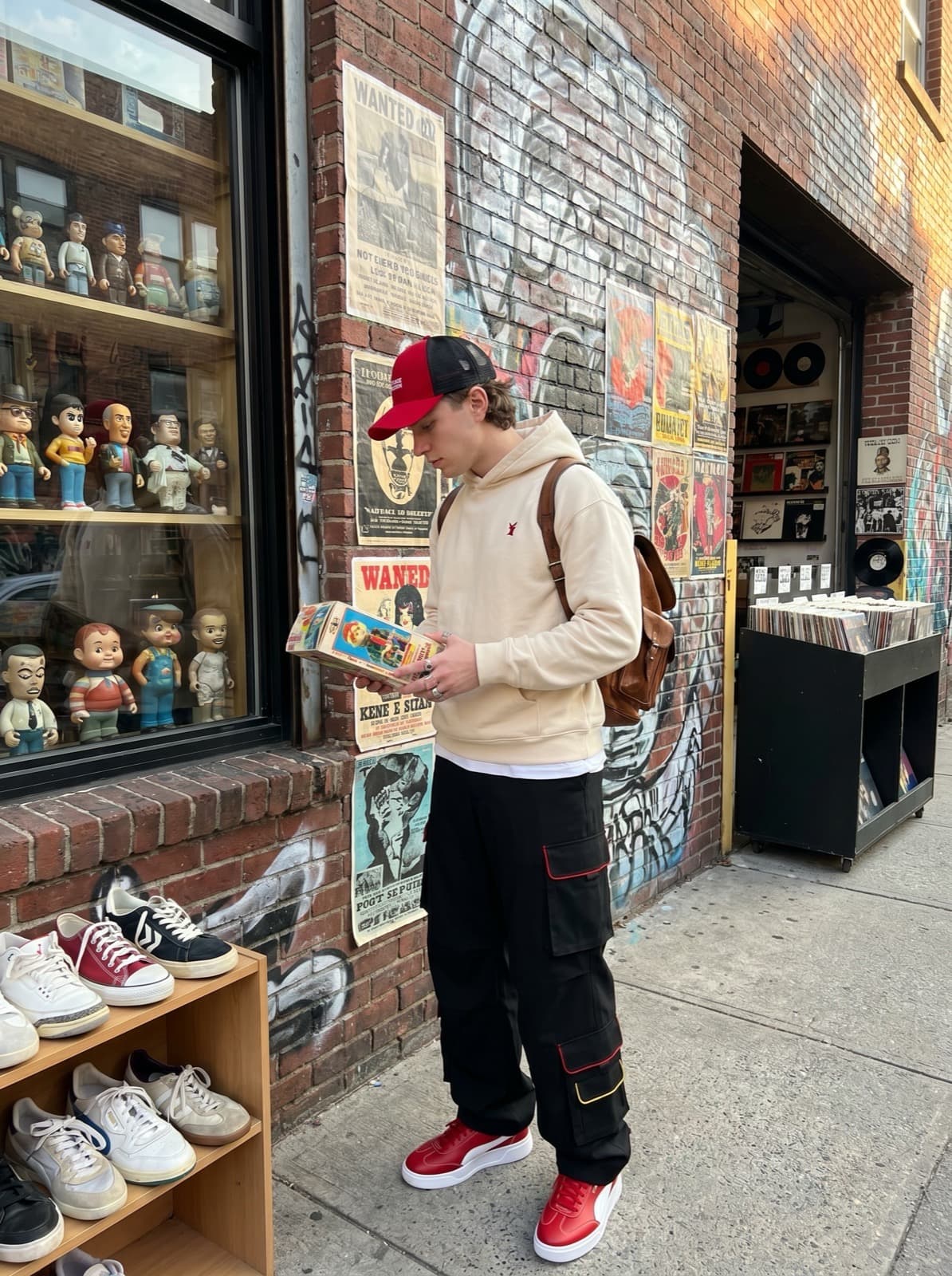 A model wearing cargo pants and an oversized hoodie outside a record store, holding a box